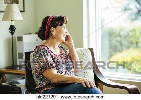 Stock Image - Caucasian woman talking on cell phone in armchair. Fotosearch