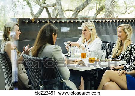 Stock Image - Caucasian woman using cell phones and drinking cocktails. Fotosearch