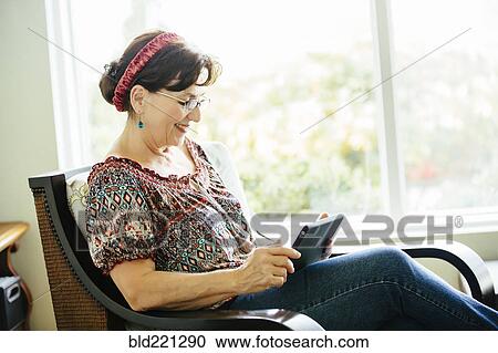 Stock Image - Caucasian woman using digital tablet in armchair. Fotosearch