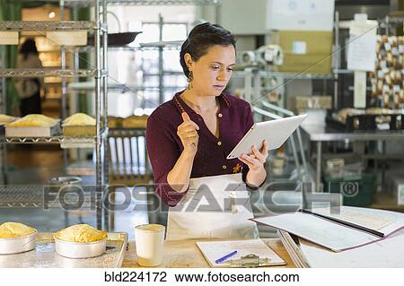Stock Image - Caucasian woman using digital tablet in bakery. Fotosearch