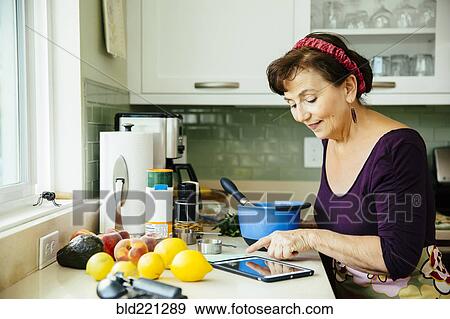 Stock Photo - Caucasian woman using digital tablet in kitchen. Fotosearch