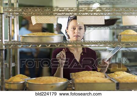 Stock Photo - Caucasian woman using digital tablet in bakery. Fotosearch