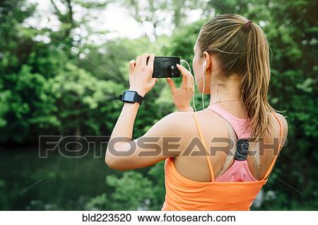 Caucasian woman using earbuds photographing with cell phone View Large Photo Image Stock Image - Caucasian woman using earbuds photographing with cell phone. Fotosearch
