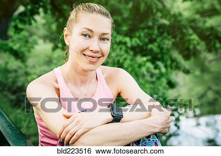 Stock Photograph - Caucasian woman wearing smart watch sitting outdoors. Fotosearch