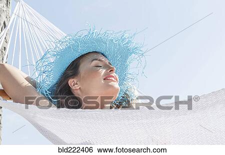 Stock Photograph - Caucasian woman wearing sun hat in hammock. Fotosearch