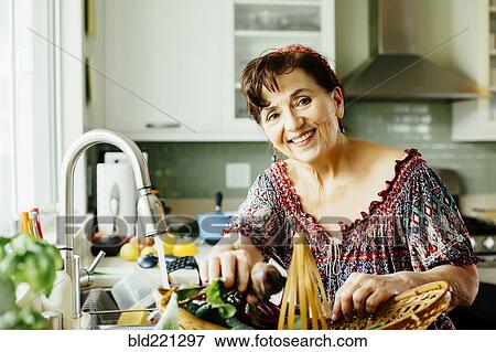 Stock Photo - Caucasian woman with produce basket in kitchen. Fotosearch