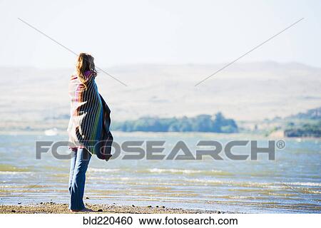 Stock Image - Caucasian woman wrapped in blanket on beach. Fotosearch