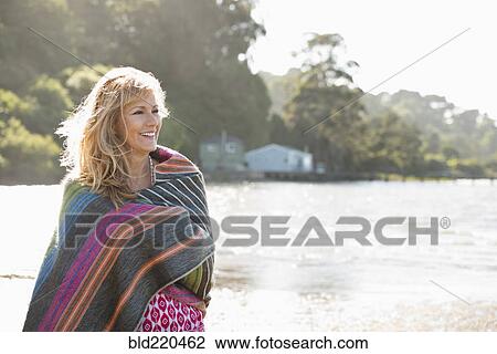 Stock Image - Caucasian woman wrapped in blanket on beach. Fotosearch