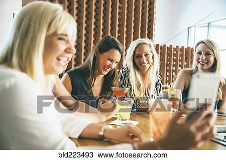 Stock Image - Caucasian women at bar with cocktails taking selfie. Fotosearch