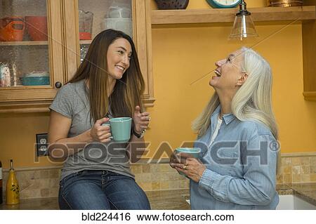 Stock Photograph - Caucasian women laughing in kitchen drinking coffee. Fotosearch