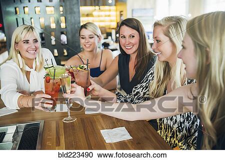 Stock Image - Caucasian women toasting at bar with cocktails. Fotosearch