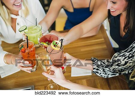 Stock Image - Caucasian women toasting at bar with cocktails. Fotosearch