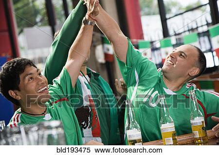 Stock Photography - Cheering Hispanic men watching television in sports bar. Fotosearch