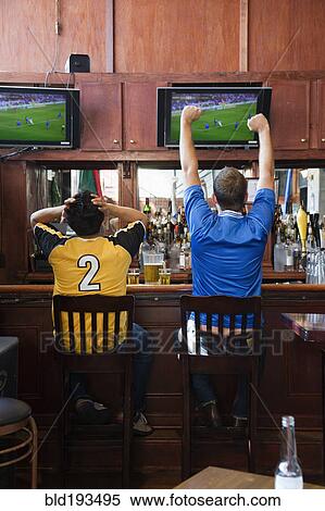 Stock Photography - Cheering men watching television in sports bar. Fotosearch