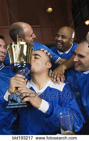Stock Photo - Cheering teammates and man kissing trophy. Fotosearch