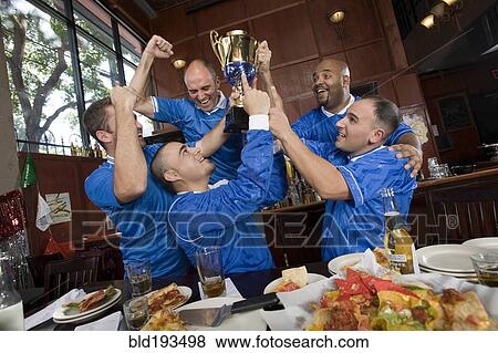 Cheering teammates and man lifting trophy View Large Photo Image Stock Photo - Cheering teammates and man lifting trophy. Fotosearch