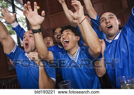 Stock Image - Cheering teammates watching television in sports bar. Fotosearch