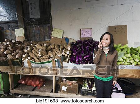 Stock Image - Chinese girl talking on cell phone at outdoor market. Fotosearch