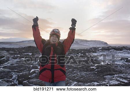 Stock Image - Chinese man standing with arms raised in remote ice field. Fotosearch