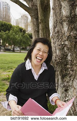 Chinese woman holding folder next to tree View Large Photo Image Stock Image - Chinese woman holding folder next to tree. Fotosearch