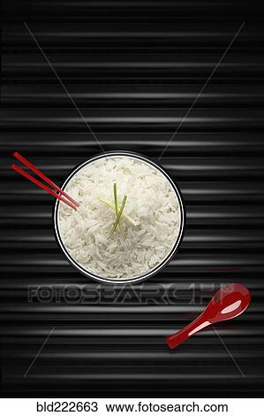 Stock Image - Chopsticks in bowl of white rice with red spoon. Fotosearch