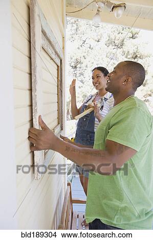 Picture - Couple attaching frame to outside of house. Fotosearch