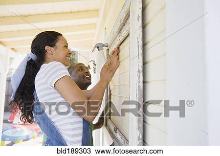 Stock Image - Couple attaching frame to outside of house. Fotosearch