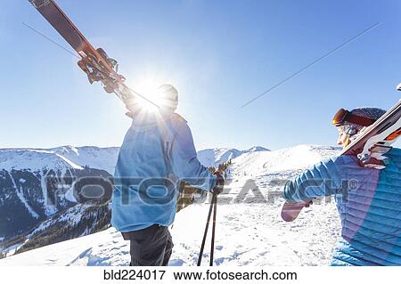 Stock Photo - Couple carrying skis on snowy mountain. Fotosearch