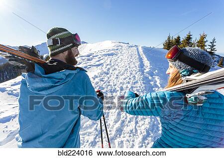Couple carrying skis on snowy mountain View Large Photo Image Stock Photograph - Couple carrying skis on snowy mountain. Fotosearch