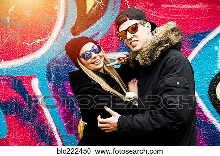 Stock Image - Couple gesturing peace at graffiti wall. Fotosearch
