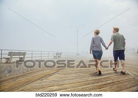 Stock Photo - Couple holding hands on wooden boardwalk. Fotosearch