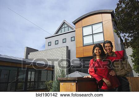 Stock Image - Couple hugging in front of modern house. Fotosearch