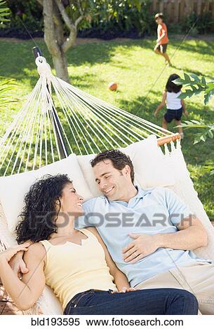 Stock Photography - Couple in hammock with children playing in background. Fotosearch