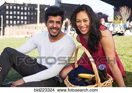 Picture - Couple sitting on grass with picnic basket. Fotosearch