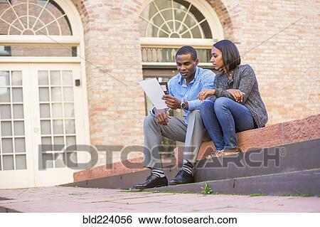 Couple sitting on steps reading paperwork View Large Photo Image Stock Photograph - Couple sitting on steps reading paperwork. Fotosearch
