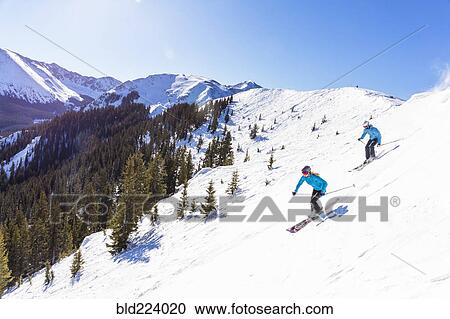 Stock Image - Couple skiing on snowy mountain slope. Fotosearch