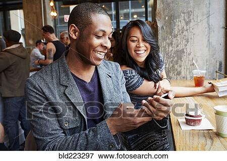Stock Photo - Couple using cell phone in cafe. Fotosearch