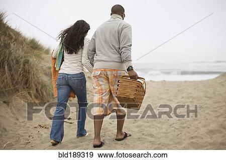 Stock Photo - Couple walking on beach with picnic basket. Fotosearch
