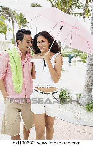 Stock Image - Couple walking with umbrella. Fotosearch