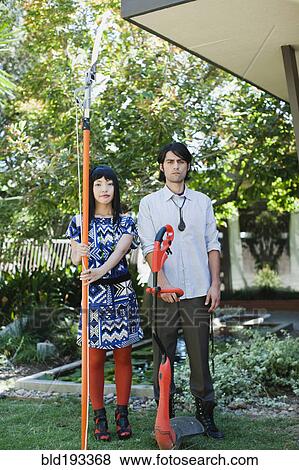 Stock Photo - Couple working in garden with tree and weed trimmers. Fotosearch