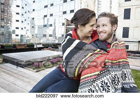 Stock Photo - Couple wrapped in blanket on urban rooftop. Fotosearch
