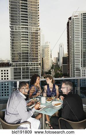Stock Photo - Couples eating dinner on urban balcony. Fotosearch