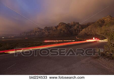 Stock Image - Curving light trails on street near mountain. Fotosearch