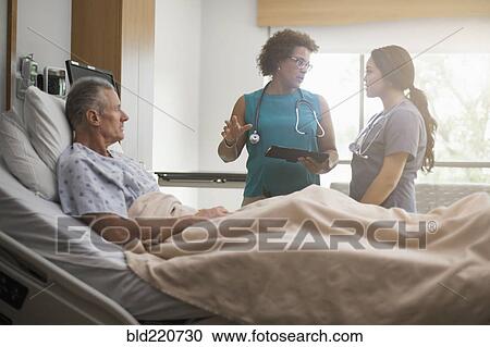 Stock Image - Doctor and nurse with patient in hospital room. Fotosearch