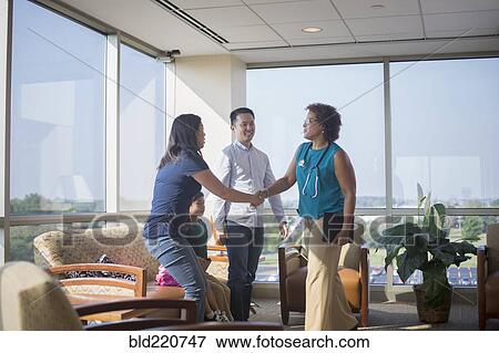 Stock Photo - Doctor greeting patients in waiting room. Fotosearch