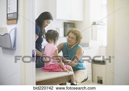 Stock Image - Doctor listening to chest of girl in hospital room. Fotosearch
