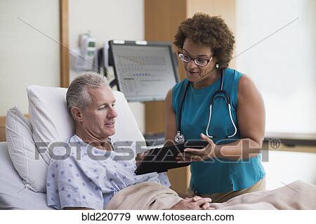 Doctor using digital tablet with patient in hotel room View Large Photo Image Stock Photo - Doctor using digital tablet with patient in hotel room. Fotosearch