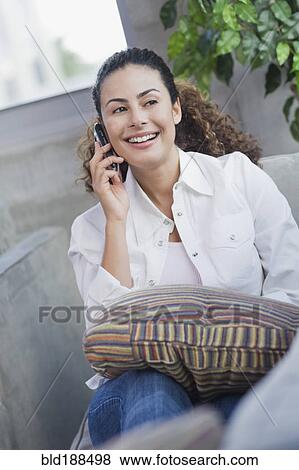 Stock Photo - Dominican woman talking on cell phone on sofa. Fotosearch