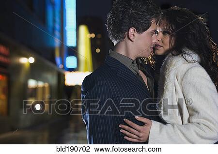 Stock Image - Elegant couple kissing on urban street at night. Fotosearch