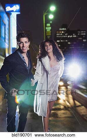 Stock Image - Elegant couple walking on urban street at night. Fotosearch